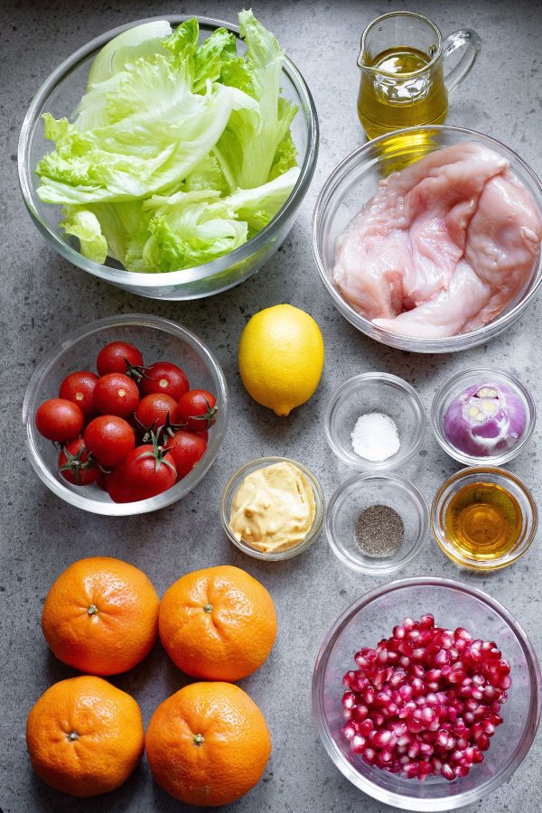 Ingredients to make mandarin orange salad with chicken and dressing measured in small glass bowls on a light gray marble table. 