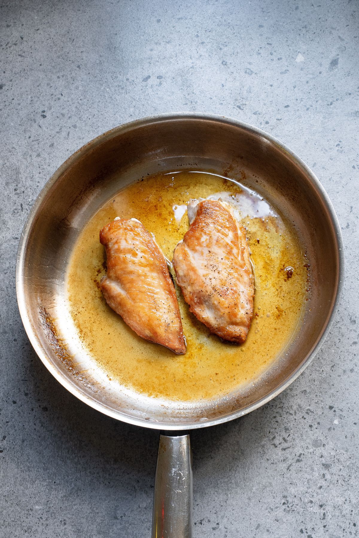 Chicken breasts fried in a frying pan with juices around them. 