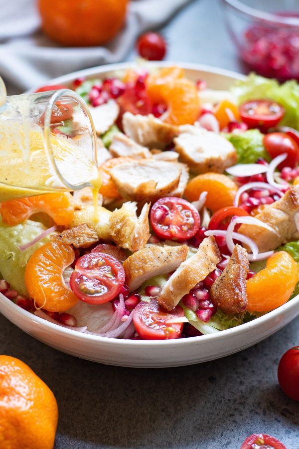 Mandarin orange chicken in a white bowl with dressing being poured over top. 