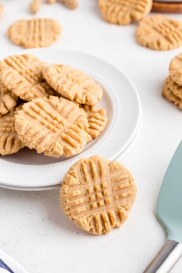 Golden peanut butter cookies on a white plate with one cookie stacked against the plates.