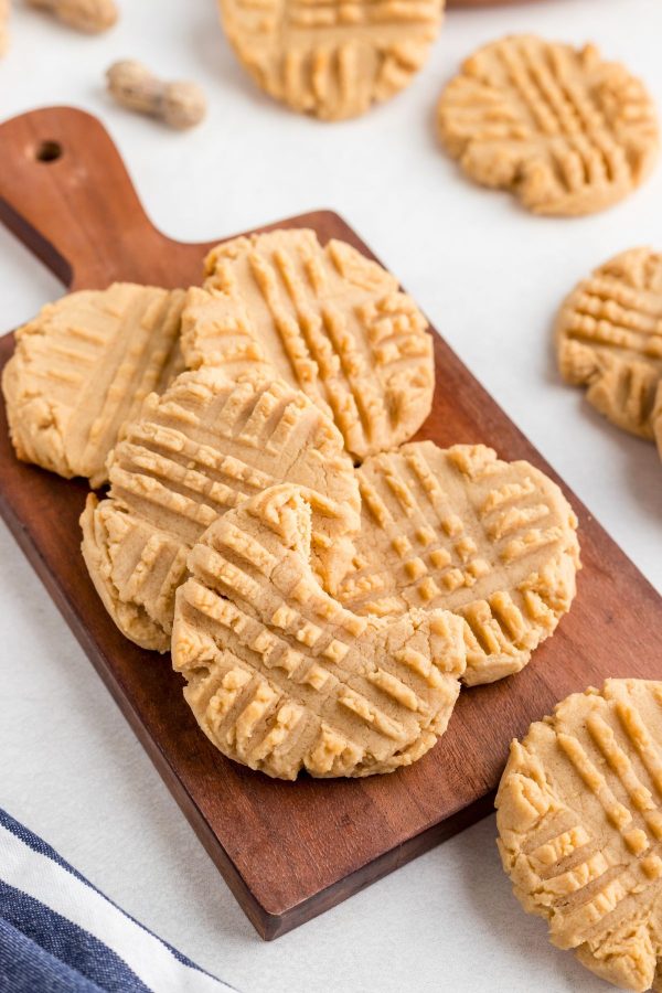 Golden cookies on a dark wood cutting board with one cookie with a bite missing. 