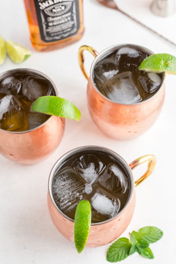 Three copper mugs filled with ice, whiskey, ginger beer and lime juice, garnished with lime  wedges.