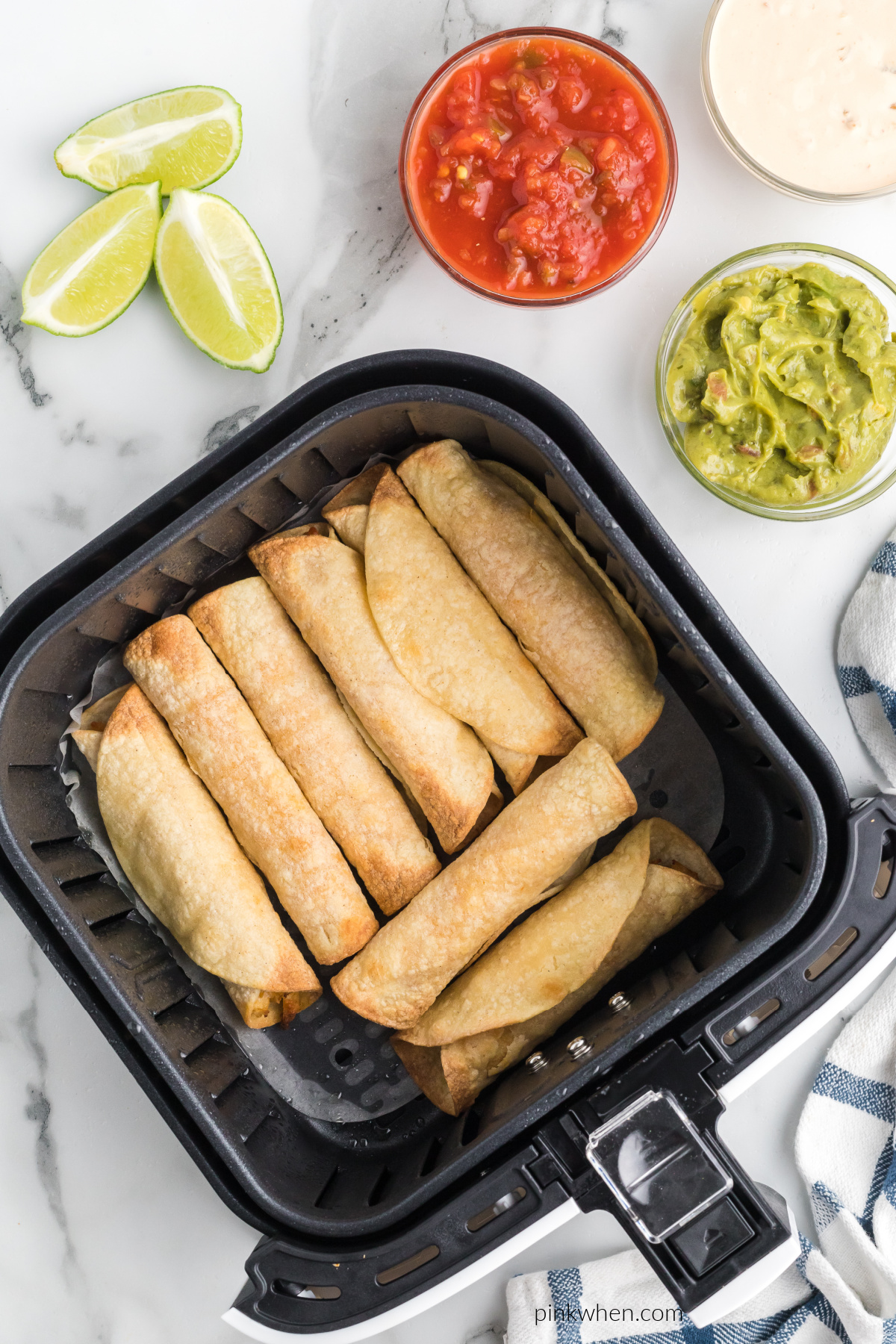 chicken taquitos in the air fryer basket and dipping sauces surrounding the basket.