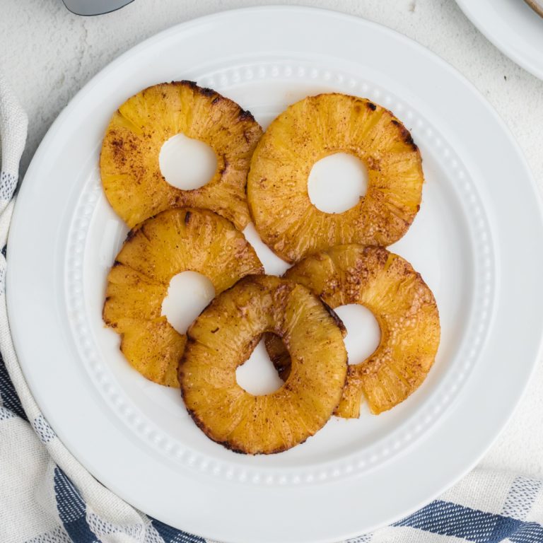 Air fryer pineapple rings topped with cinnamon and sugar and served on a white plate.