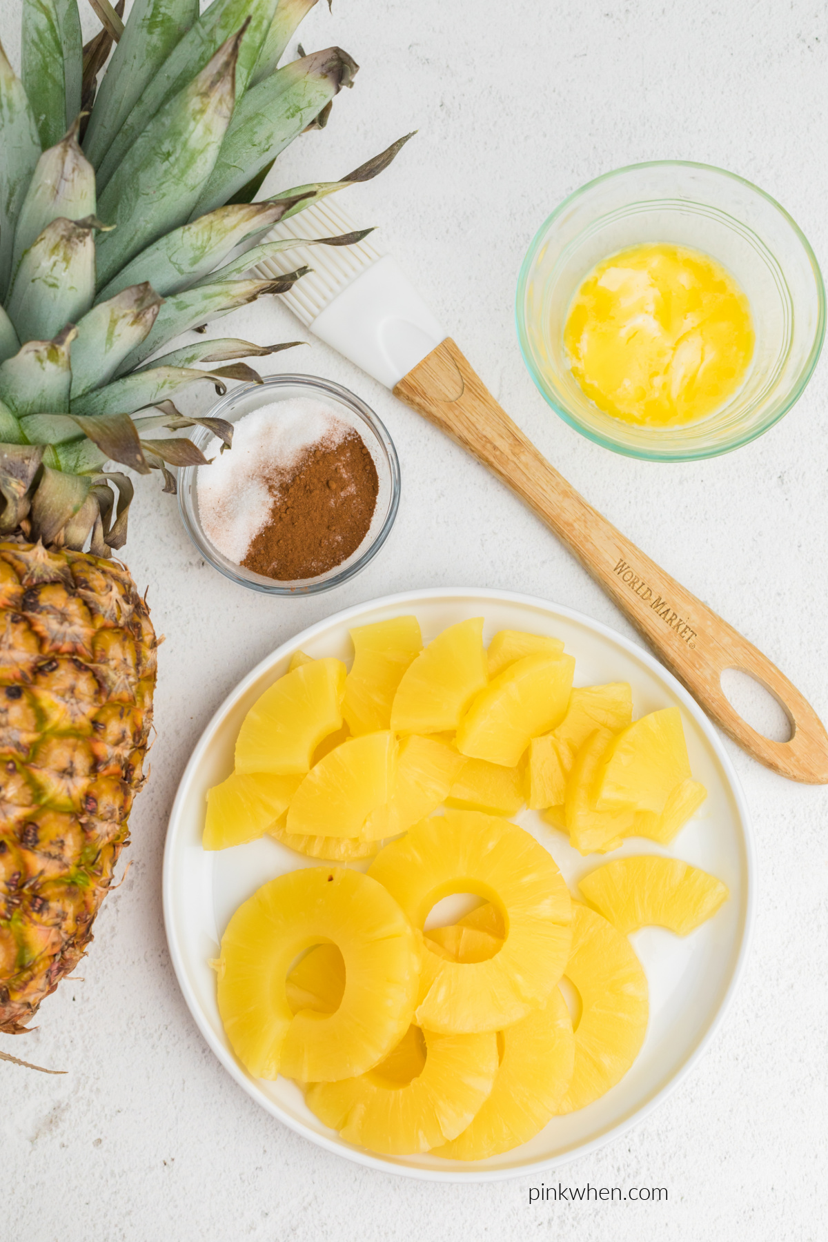 Pineapple, sugar, cinnamon, melted butter, and a basting brush on a table.