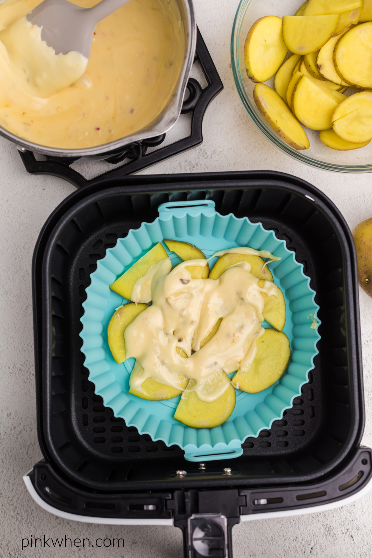 Layering potatoes and cheese in the silicone dish in the air fryer basket.