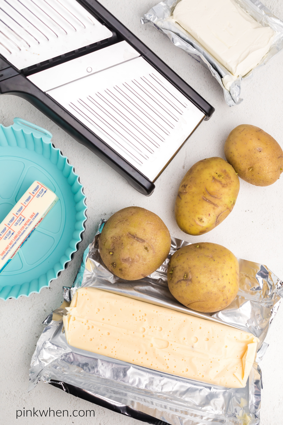 Mandolin, potatoes, queso cheese, butter, and cream cheese on a table.