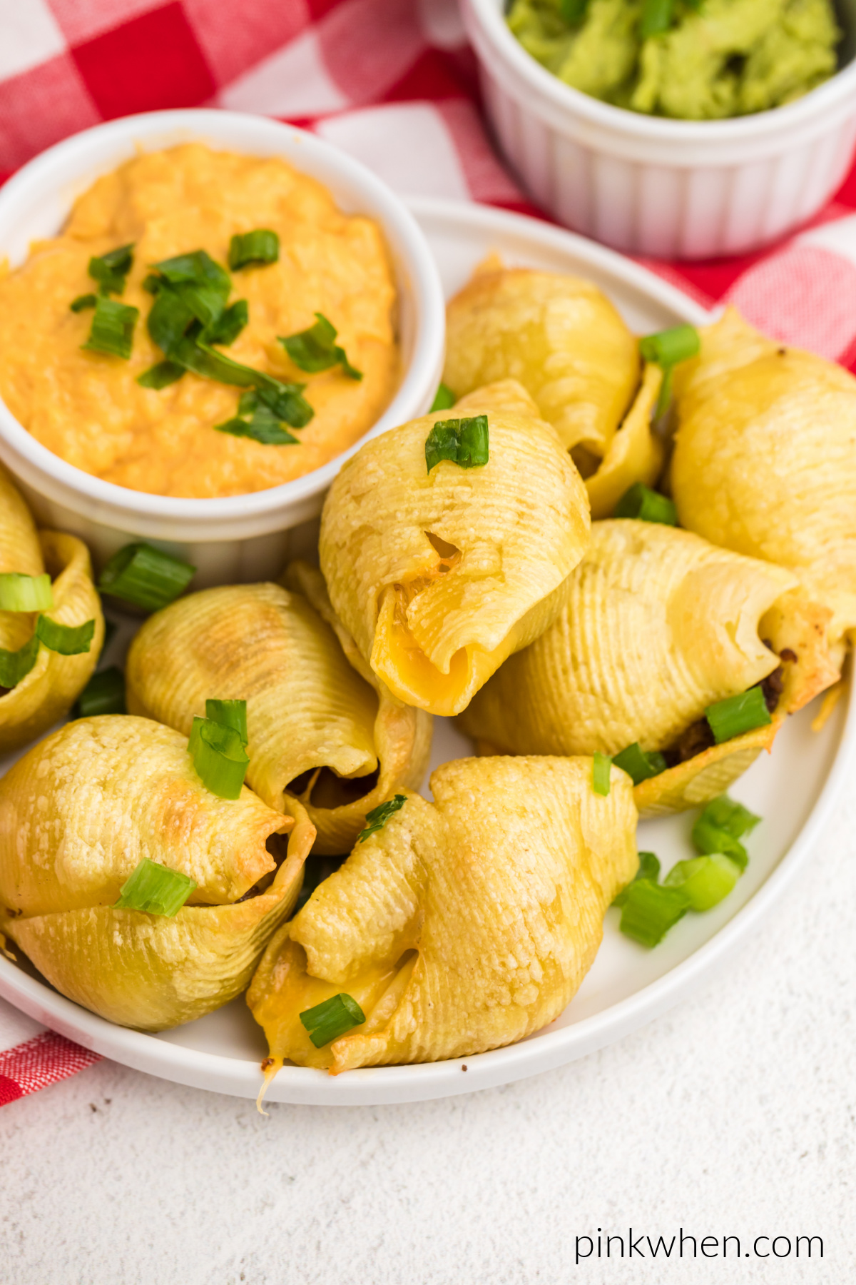 Taco stuffed shells made in the air fryer and topped with green onions, served on a plate with queso for dipping sauce.