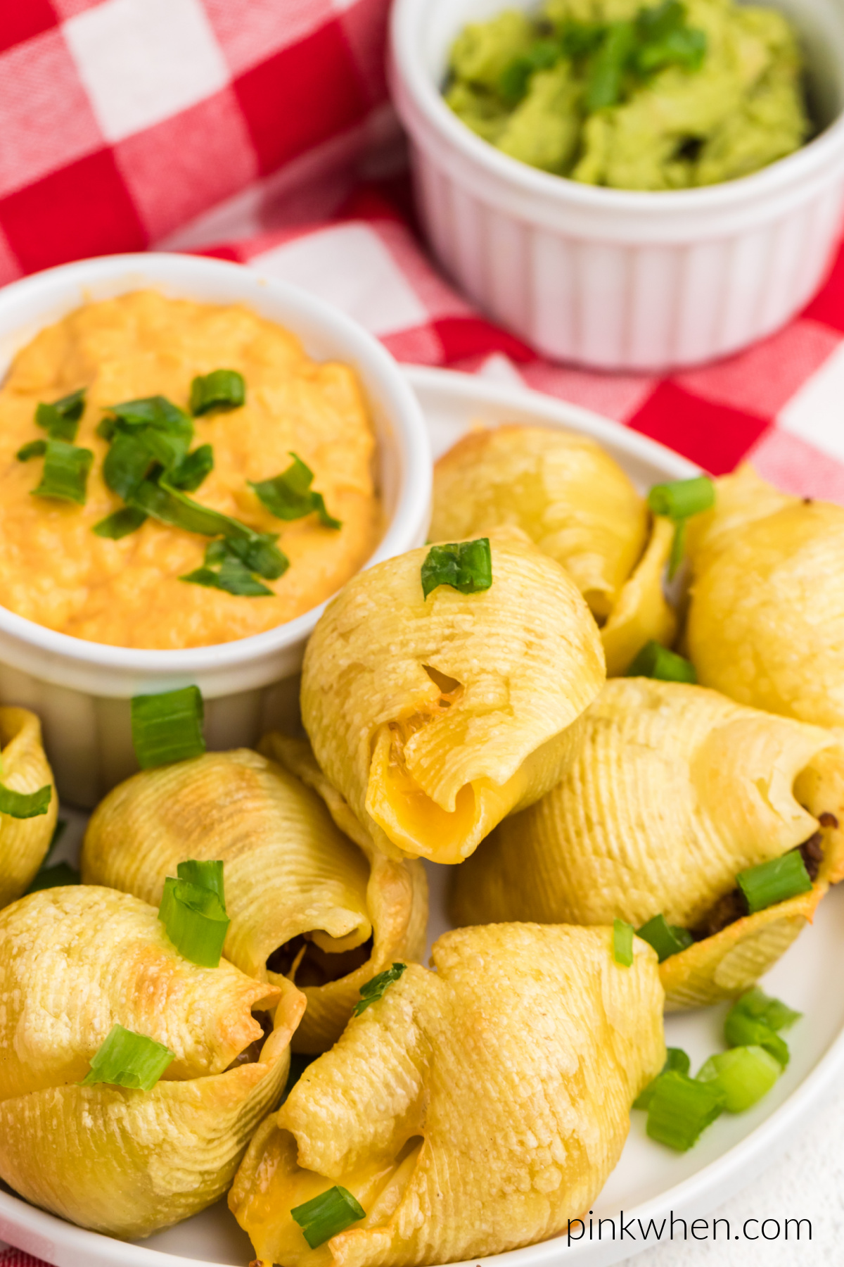 Taco stuffed shells on a white serving platter with queso and guacamole dipping sauces.
