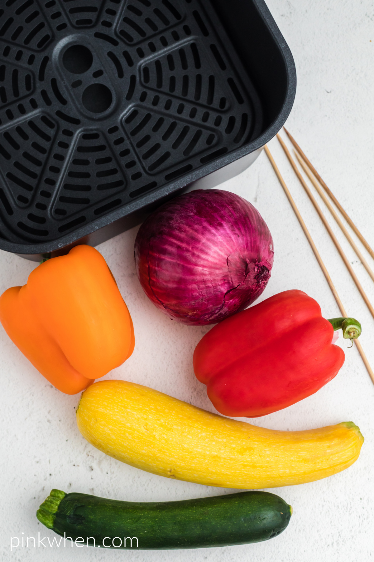 Vegetables needed to make kabobs, skewers, and an air fryer basket on a table.