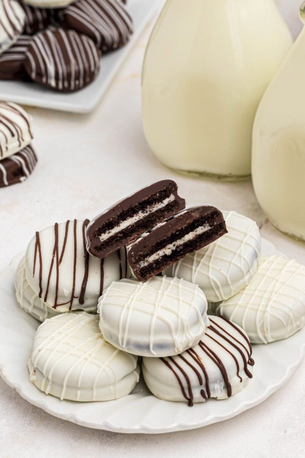 Chocolate covered Oreos and white chocolate covered Oreos on a white plate in front of milk. 