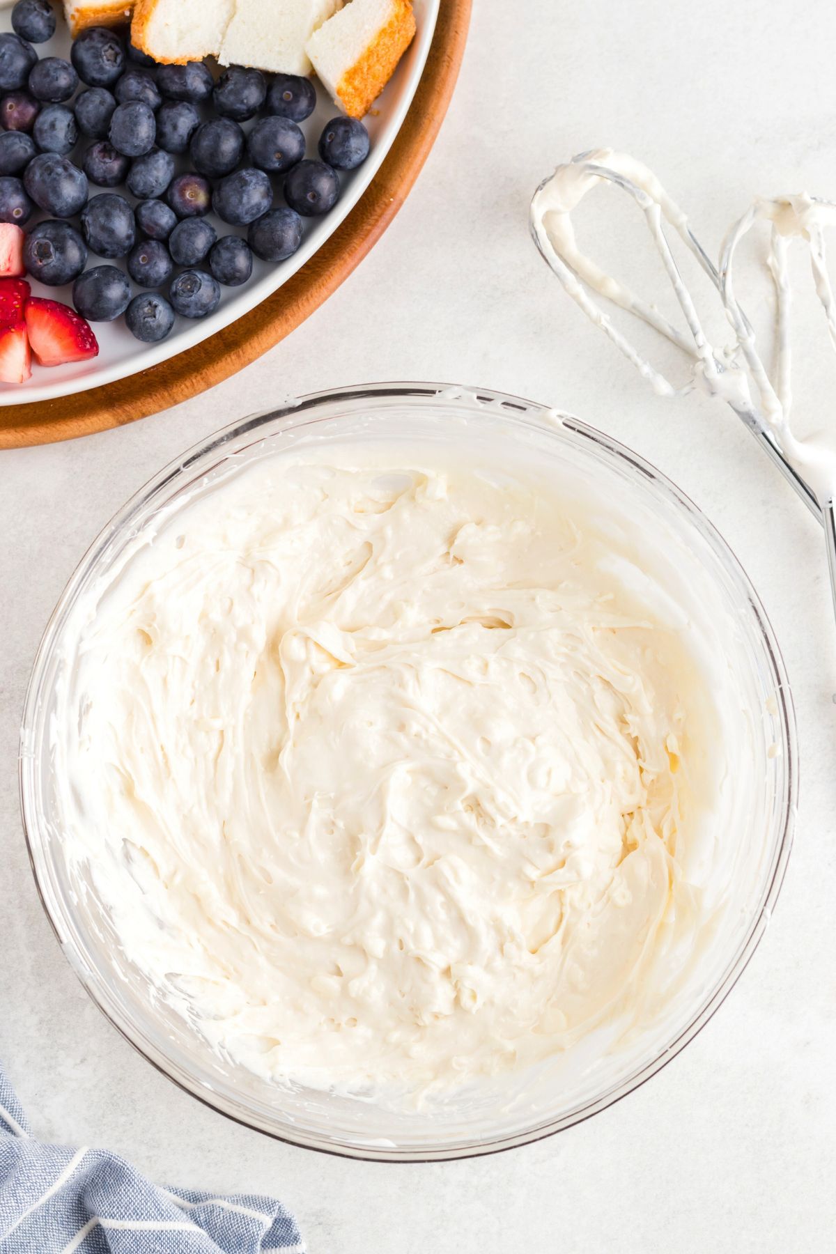 Creamy fruit dip in a clear glass bowl in front of a plate of fresh fruit. 