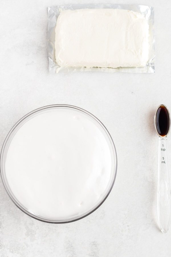 Cream cheese, marshmallow creme and vanilla measured out and on a white marble table. 