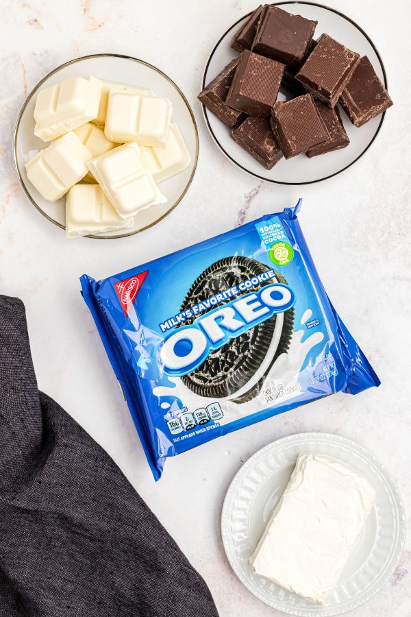 Package of Oreo cookies with cream cheese and melting chocolates on a white marble table. 