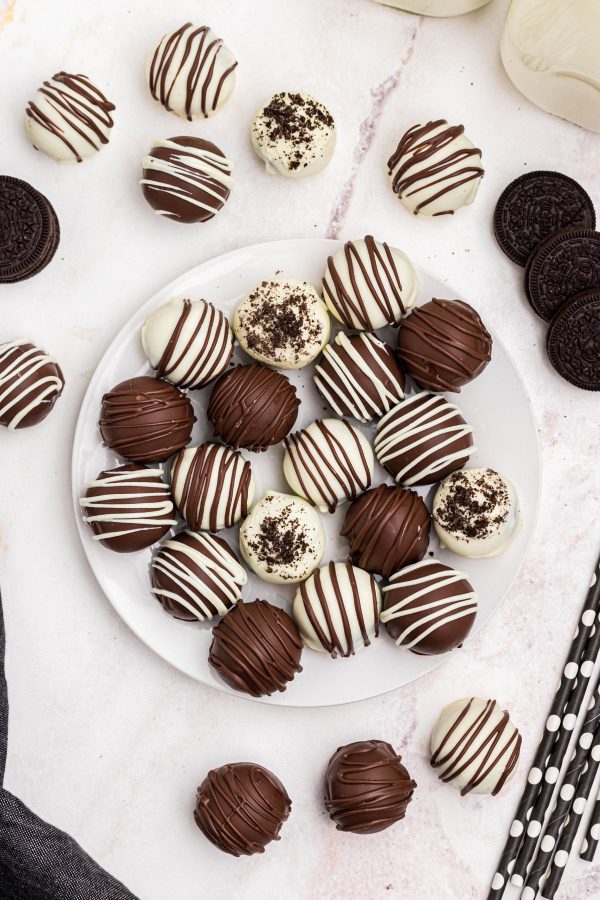 Milk chocolate and white chocolate Oreo balls on a white plate with milk and cookies on the table. 