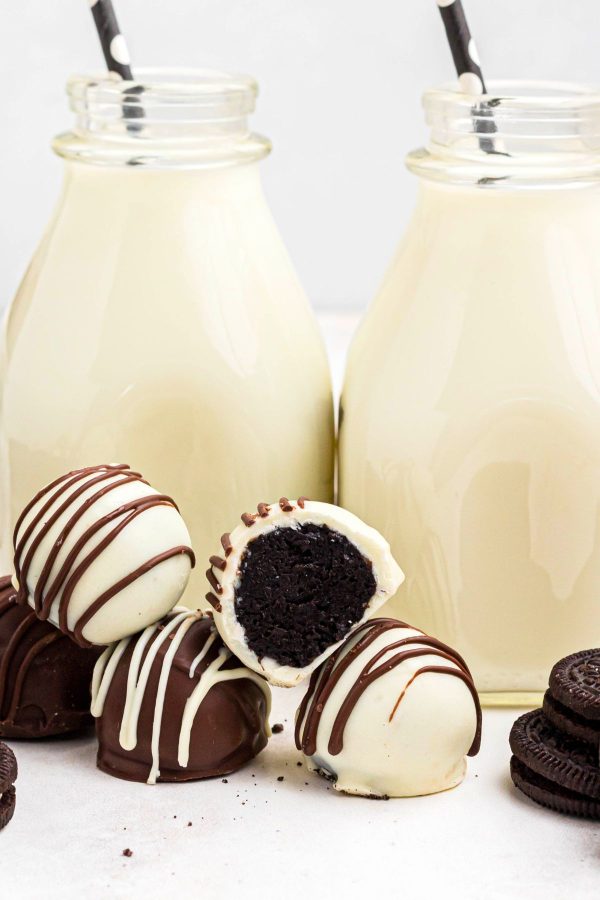 White chocolate and milk chocolate coated Oreo balls on a marble table in front of milk