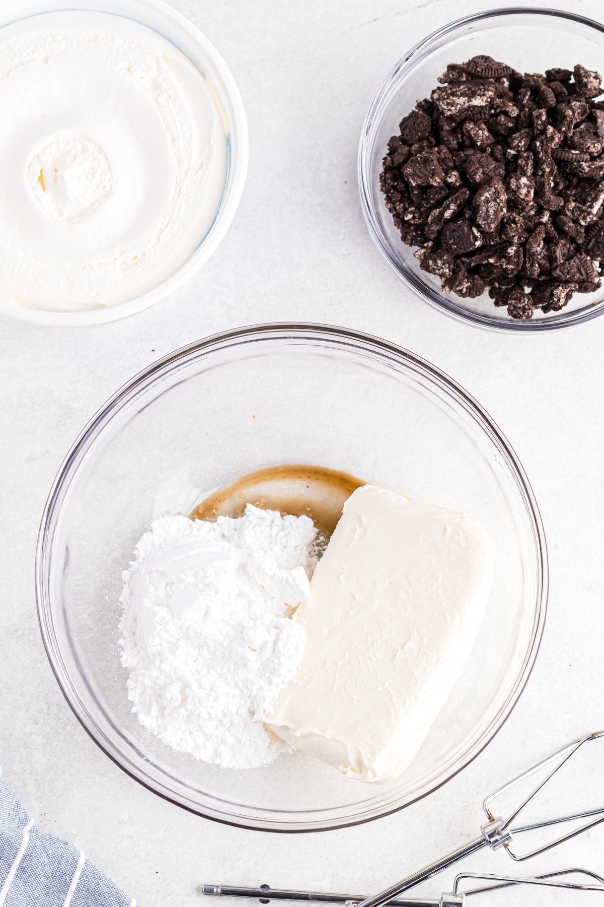Cream cheese being mixed with sugar and vanilla in a clear glass bowl. 