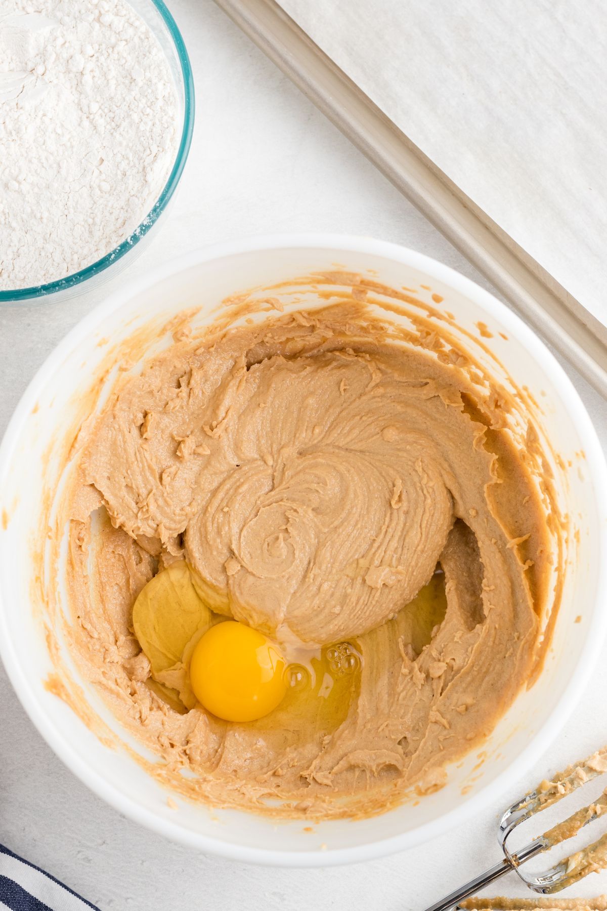 Eggs being added to dough mixture in a white mixing bowl. 