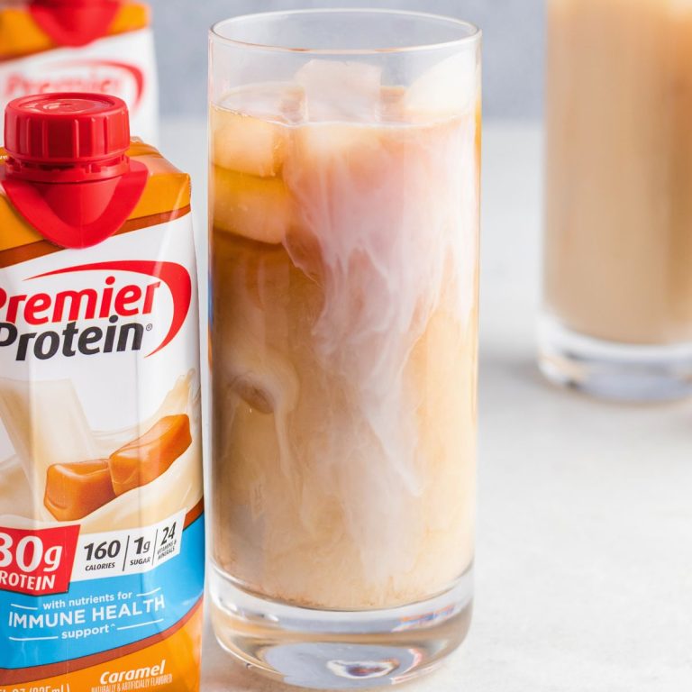 Clear glass of iced coffee with bottle of protein shake next to it on a white table.