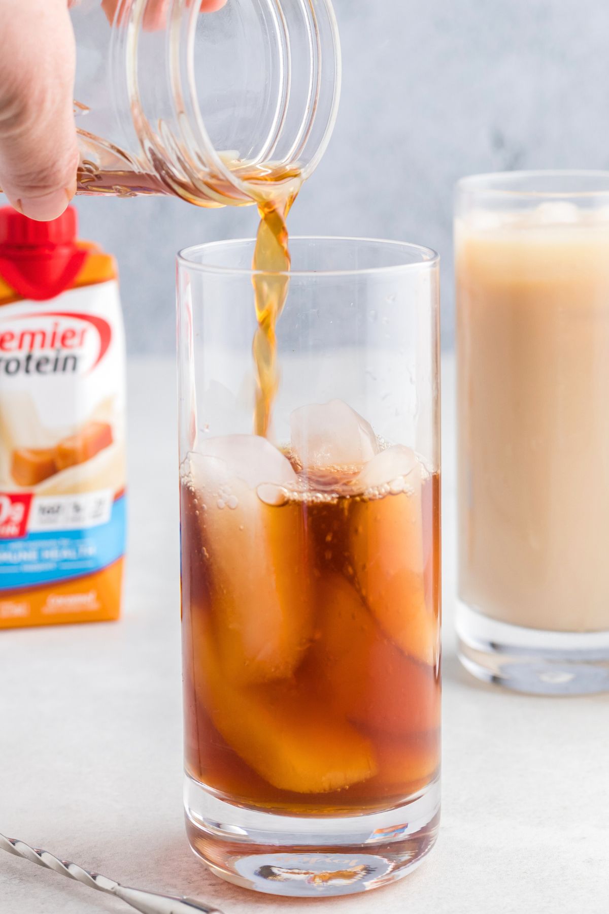 Chilled coffee being poured over ice cubes in a clear glass.