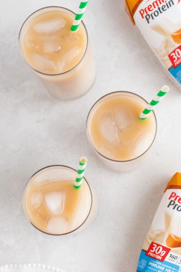 Overhead photo of three clear glasses filled with iced coffee on a white marble table. 
