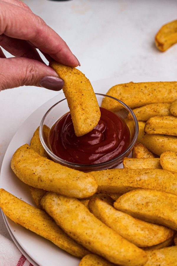 Golden seasoned Red Robin steak fries on a white plate with one being dipped into a small bowl of ketchup.
