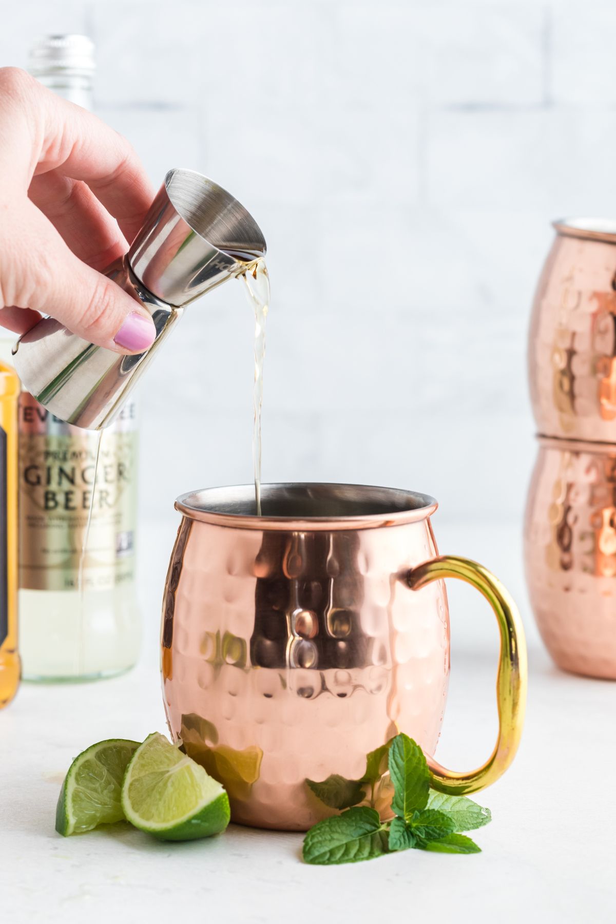 Copper mug being filled with whiskey with lime garnish on a marble table. 
