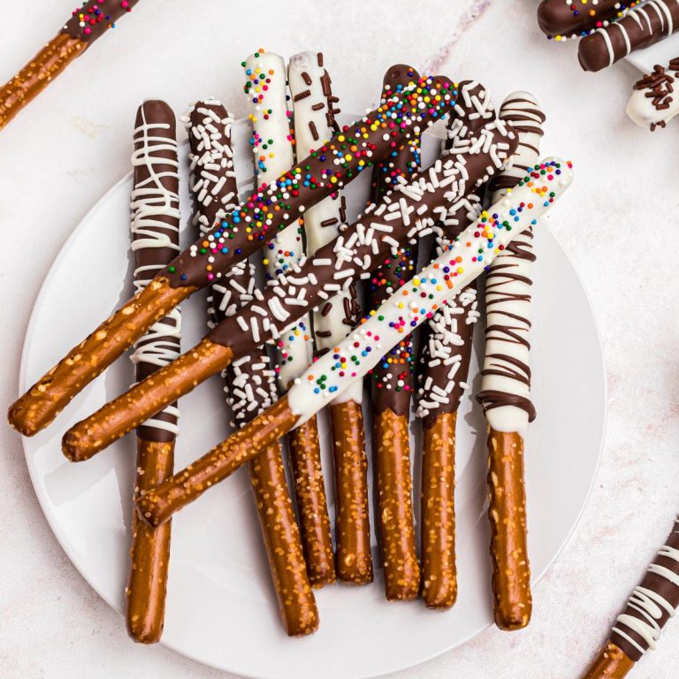 Chocolate and white chocolate coated pretzel rods with sprinkles on a white plate.