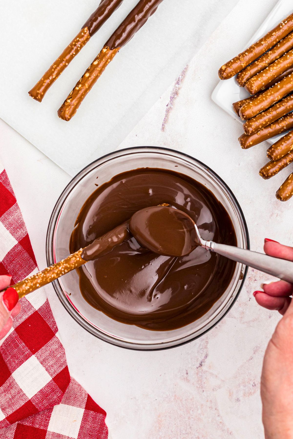 Melted chocolate in a clear glass bowl with a pretzel rod dipped into the bowl. 
