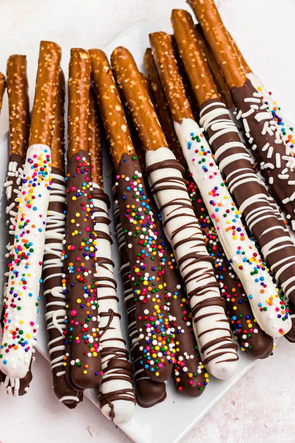 Chocolate and white chocolate dipped pretzels with sprinkles and drizzles on a white square plate. 
