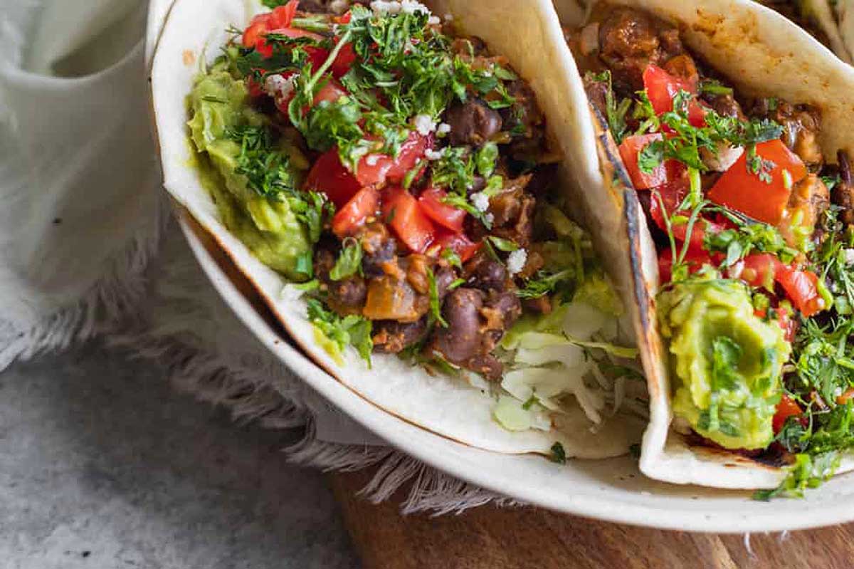 Three black bean tacos on a wooden cutting board.