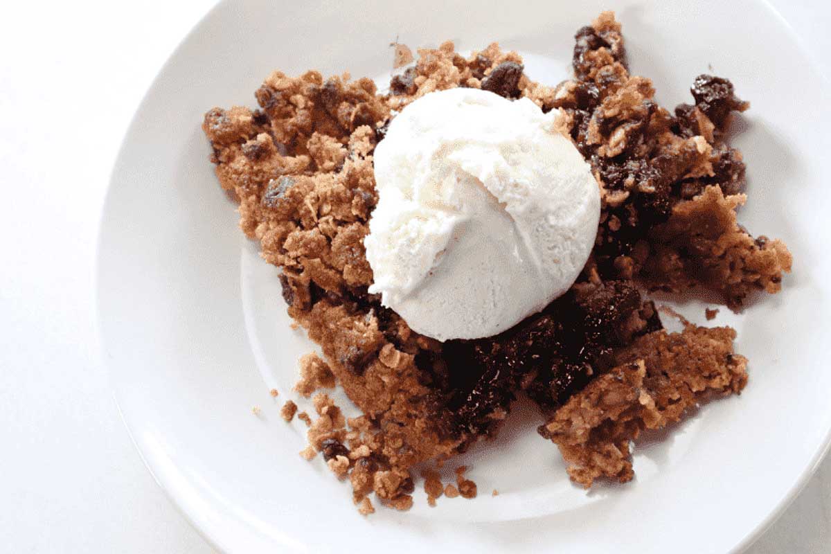 Blueberry crisp on white plate with ice cream on top.
