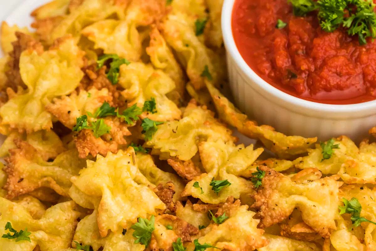 A plate full of air fried pasta chips and a bowl of marinara sauce.