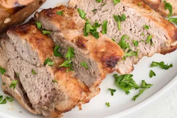 Air fryer pork tenderloin on white plate with fresh herbs.
