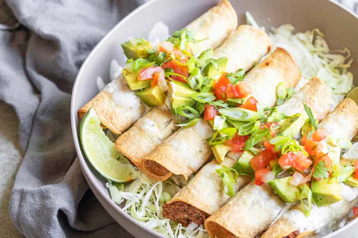 Crispy black bean taquitos with tomatoes and cabbbage.