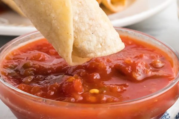 A tortilla being dipped into a bowl of salsa.