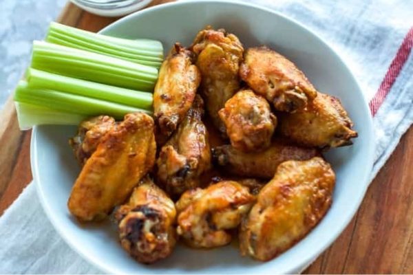 Chicken wings in a white bowl with celery.