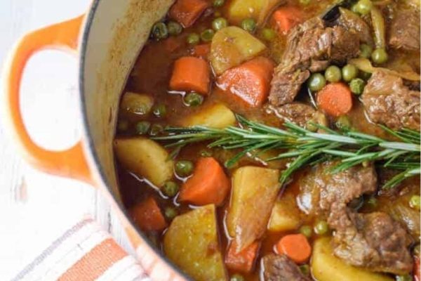 Beef stew in an orange pot with potatoes and carrots.