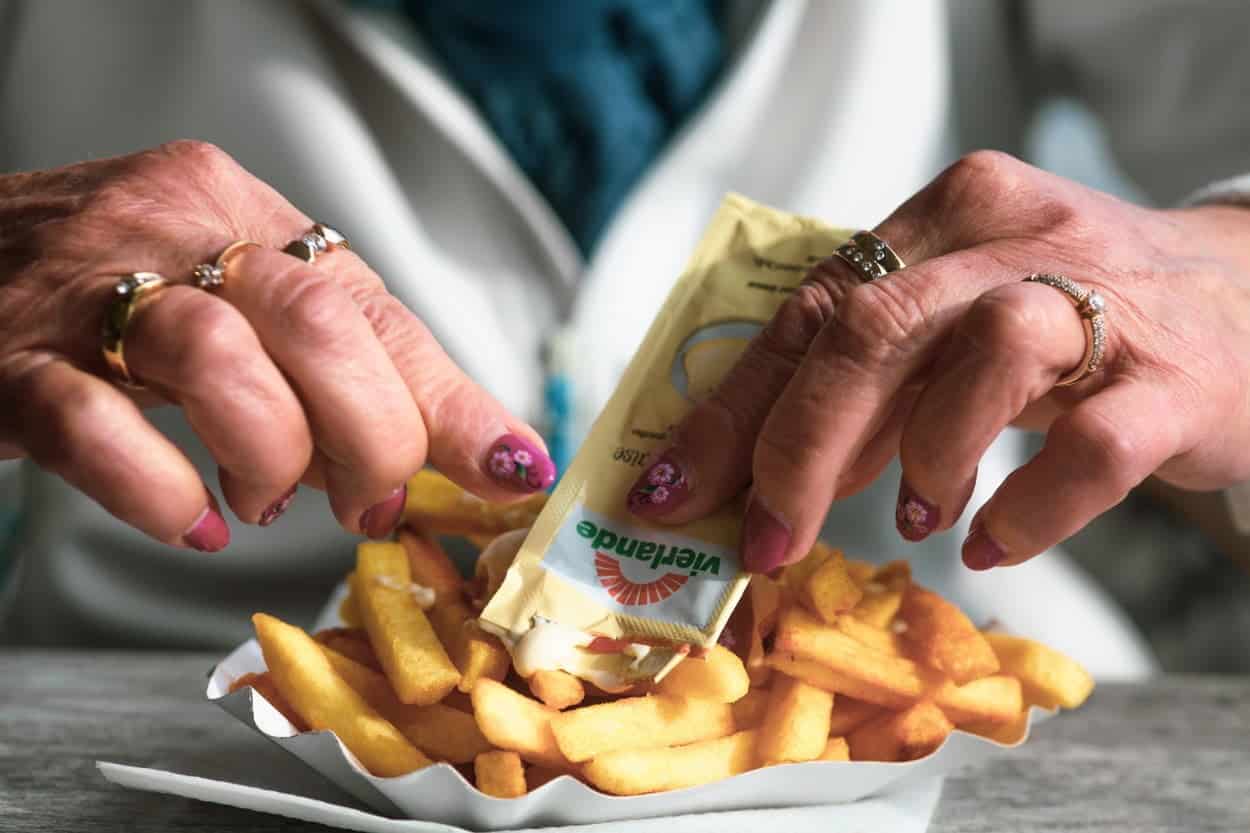 Woman squeezing a packet of sauce on top of Belgium's Pomme Frites.