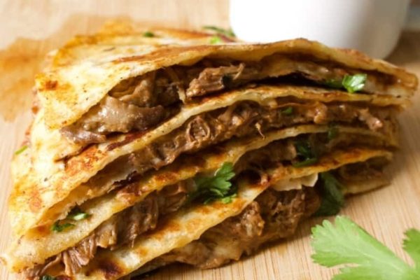A stack of meat quesadillas on a cutting board.