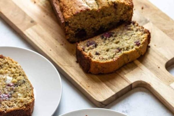 A whole loaf of Blackberry Banana Bread on a wooden chopping board.
