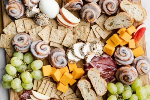A charcuterie board filled with breakfast staples such as cheese, cracers, breads, and fruits.