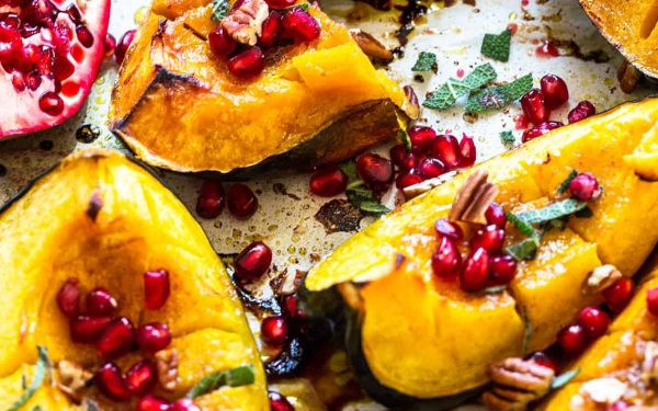 Roasted squash on a sheet pan with pomegranate seeds.