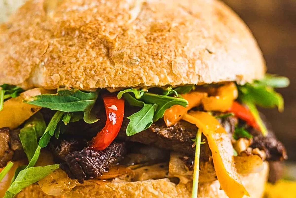 A steak sandwich with peppers served on a bun.