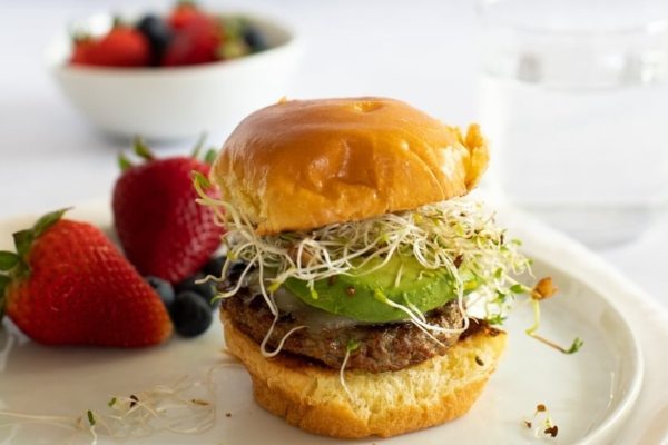 A burger with avocado and sprouts on a plate.