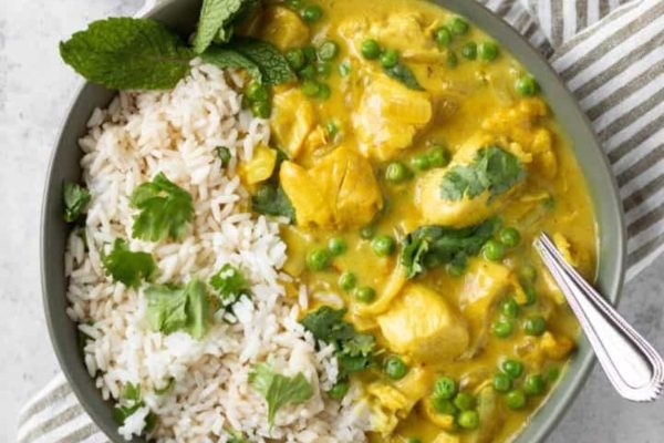 A bowl of chicken curry with rice and peas.