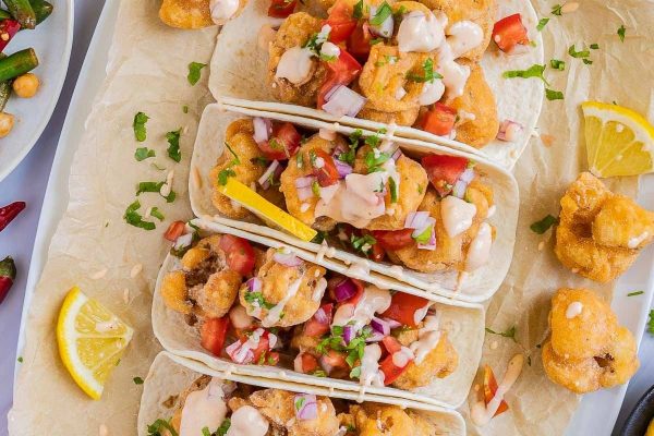 Cauliflower tacos on a white plate with lemon wedges.