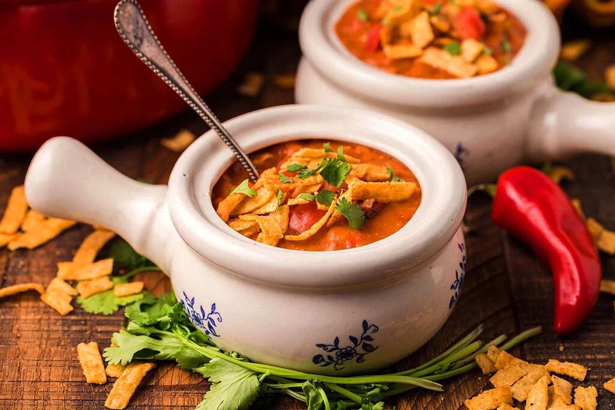 A chicken enchilada soup in bowls with tortilla strips on top.
