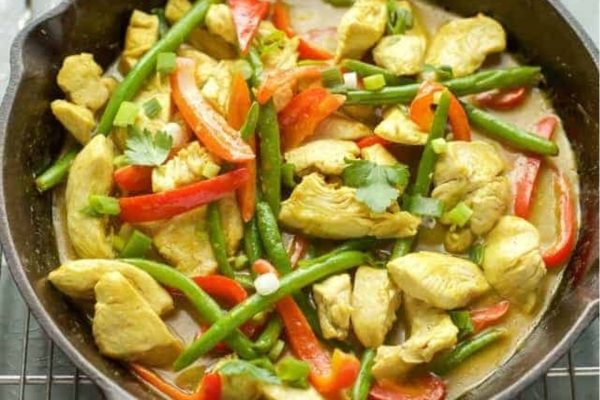 Thai chicken curry with red peppers and green beans served with slices of green onion over the top.