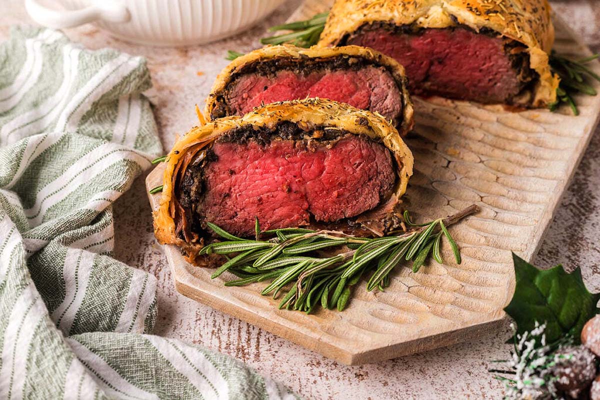 A beef wellington sliced and on a cutting board.